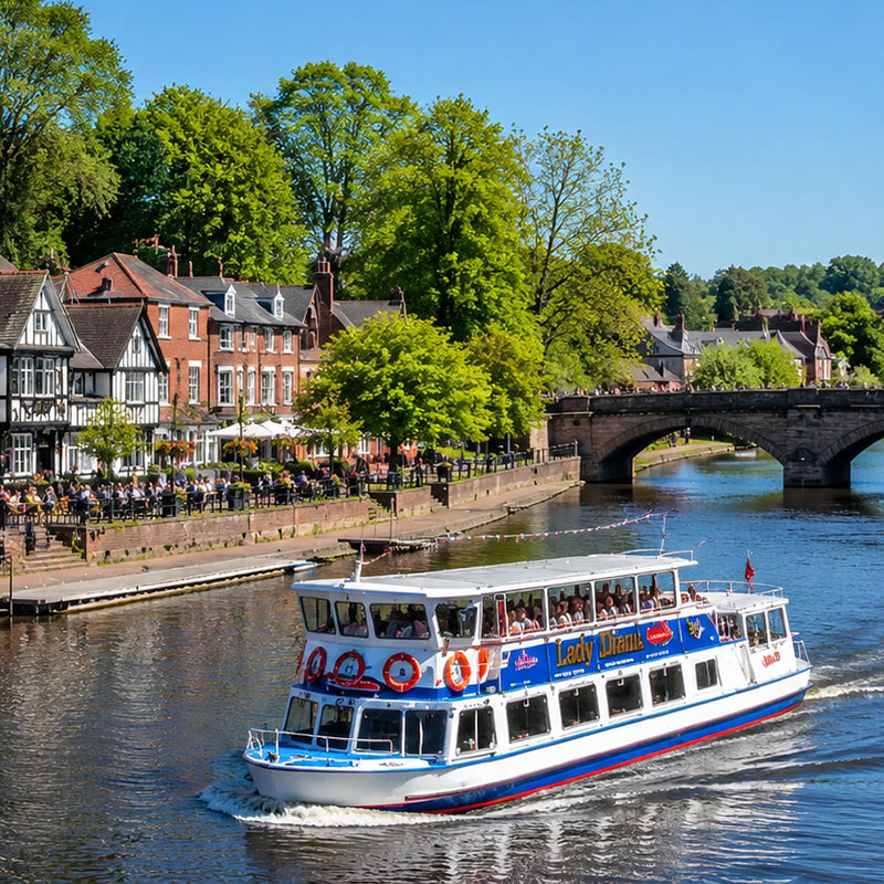 A river cruise boat on the River Dee in Chester, with Tudor buildings along the bank