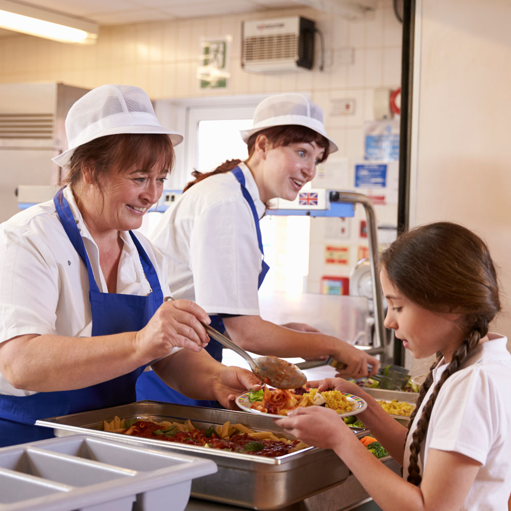 Two female lunchtime assistants serving lunch to school children