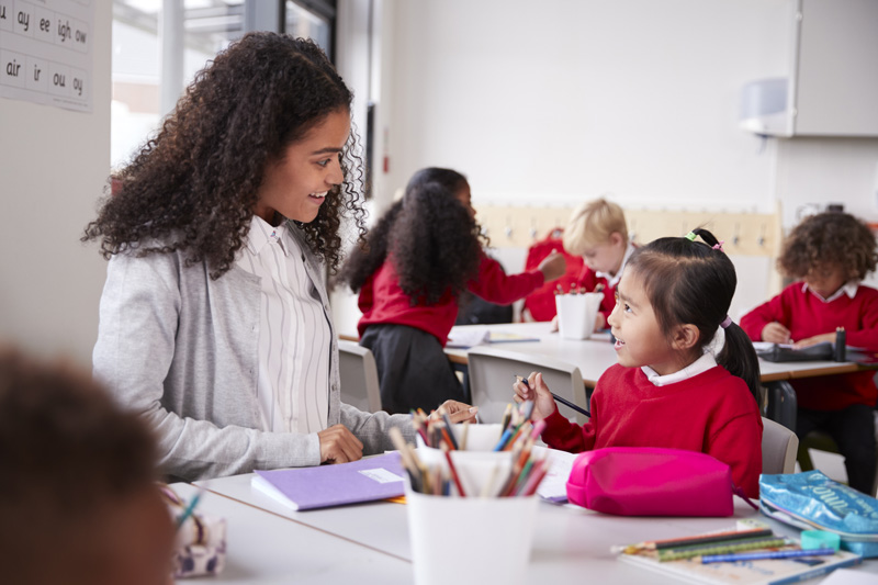 Female teaching assistant with a young pupil discussing class work